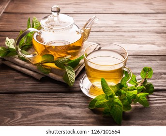  Fragrant Fresh Herbal Tea Of ​​mint And Melissa In A Glass Cup And A Teapot On A Dark Wooden Background. Traditional Herbal Drink. Place For Text Or Design.