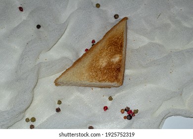 Fragrant Freshly Baked Bread In The Shape Of A Triangle. A Slice On A White Napkin With Scattered Peppercorns.