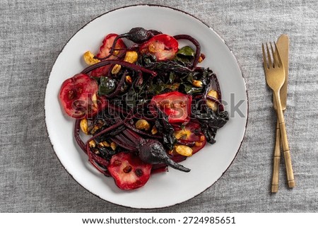 A fragrant and nutritious salad of roasted beetroot stalks and leaves, apple slices, garlic, peanuts and raisins, served on a white plate, close up