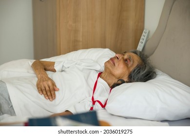 Frail old Indian Asian woman lying in bed in a hospital room or nursing home, UK.