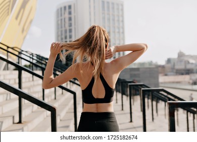 Frame from back of athletic girl wearing sport uniform training outside in sunlight in the city. Fitness sport woman in fashion sportswear doing yoga fitness exercise in the city