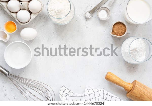 Frame of baking and cooking\
bread pastry or cake ingredients, flour sugar milk eggs and coconut\
butter on bright grey background with copy space for text, flat\
lay
