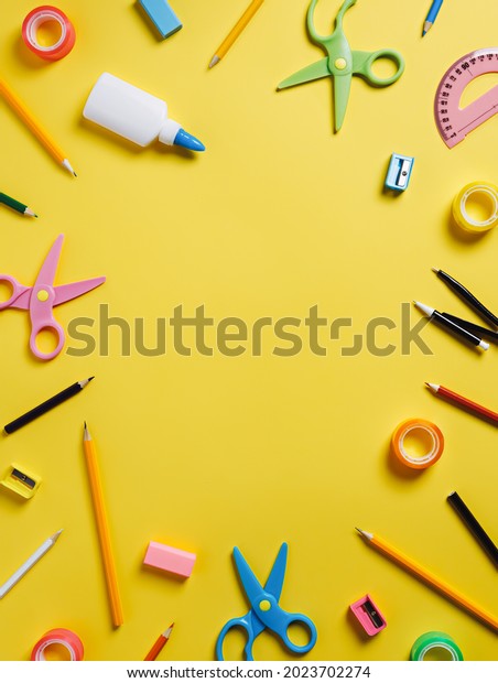 Frame border with school and office equipment on\
yellow background. Glue, pens, scissors, divider, office\
accessories and ruler with copy space for text. Creative back to\
school concept. Flat lay.