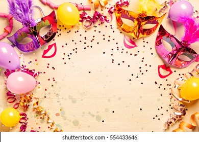 Frame of brightly colored metallic Mardi gras masks, red lips and streamers with scattered confetti and balloons with copy space for your carnival greeting or advertising