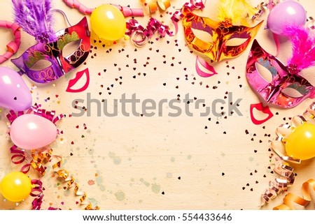 Frame of brightly colored metallic Mardi gras masks, red lips and streamers with scattered confetti and balloons with copy space for your carnival greeting or advertising