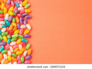 Frame of colorful jelly beans over orange background with copy space.