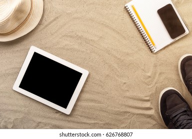 Frame from a digital tablet, notepad and clothes on the sand, top view