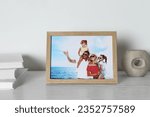 Frame with family photo, books and other decor element on white wooden table indoors