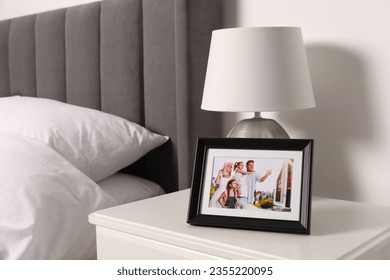 Frame with family photo and lamp on white bedside table in bedroom - Powered by Shutterstock