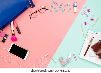 Frame flatlay with woman's blue purse, glasses, smartphone with black copyspace, cosmetics and stationery supplies. Pastel pink and mint background, business mockup, women work bag contents