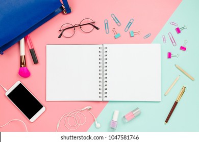 Frame flatlay with woman's purse, glasses, smartphone with black copyspace, cosmetics, stationary supples and notebook with blank white page. Pastel background, business mockup, women bag contents