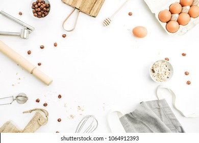 Frame of food ingredients on white background. Cooking flat lay, top view concept. Eggs, apron, cutting board, hazelnut, cereals on white background. Mock up.