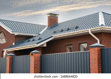 Frame house under construction with a gutter system on a metal roof. Brick chimney pipe. Automatic metal gates. - Shutterstock ID 1688064820
