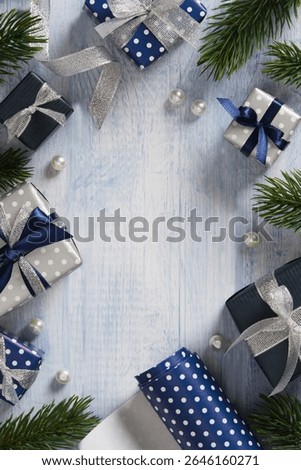 A frame made of fir branches, gift boxes, ribbons, and wrapping paper in blue and silver colors. Space for your text.