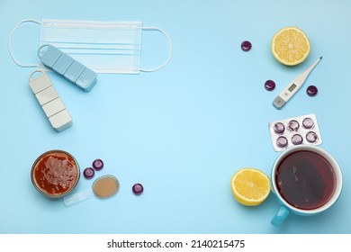 Frame Made Of Medications For Sore Throat, Tea Cup, Lemons, Jam And Thermometer On Blue Background