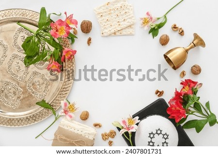 Frame made of Passover Seder plate, flatbread matza, kippah, wine cup, walnuts and flowers on white background