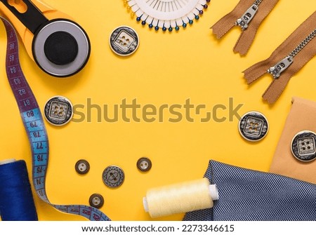Frame made of sewing tools on a yellow background. Roller cutter, bobbins, zippers, buttons, textile, measuring tape. Flat lay. Copy space.