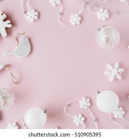 frame made of white christmas decoration with christmas glass balls, tinsel, bow, elk, bird on pink background. christmas wallpaper. flat lay, top view