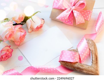 Frame of pink roses, gift box, wooden heart, pink ribbon polka dots, blank empty sheet on white. - Powered by Shutterstock