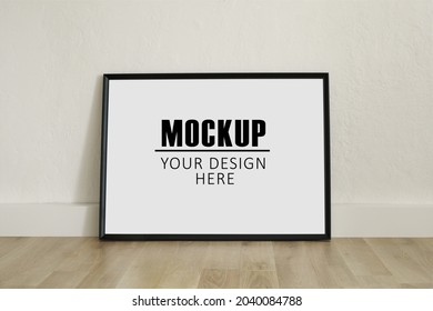 Frame, poster mock up with horizontal black frame. Empty frame standing on the wooden floor. Free space for your picture or text, copy space. Minimalist design.