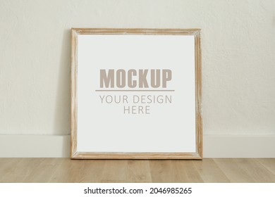 Frame, poster mock up with wooden frame. Empty frame standing on the wooden floor, white wall. Free space for your picture or text, copy space. Minimalist design
