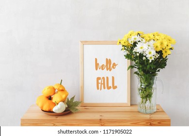 Frame With Text HELLO FALL, Plate With Squashes (bush Pumpkins) And Vase With White And Yellow Chrysanthemums On A Wooden Table On A Background Of Light Gray Walls. Autumn Home Interior Decor.