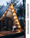 A frame triangle holiday house in the woods at night, peaceful weekend getaway in nature. Photo of an A frame triangle shape log home in the woods, peaceful weekend getaway in nature green forest