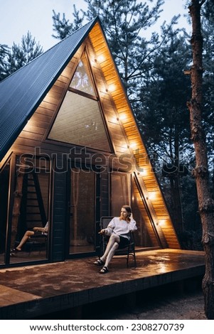 A frame triangle holiday house in the woods at night, peaceful weekend getaway in nature. Photo of an A frame triangle shape log home in the woods, peaceful weekend getaway in nature green forest