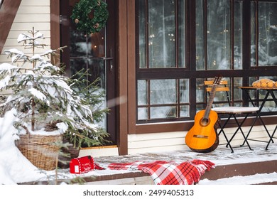 A frame triangular countryside house in the village in winter. Snowy sunny day, Christmas festive decorations outdoor. Cozy fireplace outside - Powered by Shutterstock