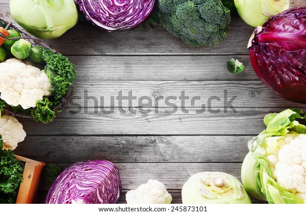 Frame of various brassica\
cabbage family varieties with cauliflower, kohlrabi, kale, cabbage\
and brussels sprouts over a rustic wooden background with\
copyspace