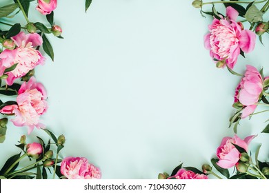 Frame wreath of pink peony flowers, branches, leaves and petals with space for text on blue background. Flat lay, top view. Peony flower texture.