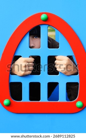 Framed by fun! Bright primary colors highlight a child's intense blue gaze and gripping hands from inside a playground structure. A world of imagination awaits! 