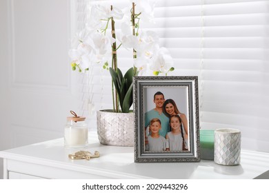 Framed family photo and orchid flower on white table indoors