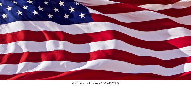 a frame-filling horizontal rendition of the U.S. flag in deep blue and red in bright sunlight and flying in a stiff breeze