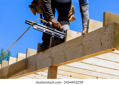 Framer worker installing beams using air nails hammer in nailing wooden frame