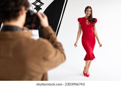 Framing elegance. Professional young man photographer capturing portraits of stylish lady, posing in photostudio on white background with modern lighting equipment