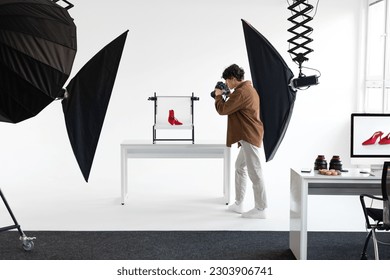 Framing the perfect shot. Male photographer taking photos of red shoes, working in modern photostudio, making content photoshoot, full length shot