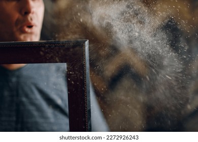 Framing Workshop. Master blows off dust baguette handmade picture frame at studio.