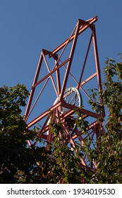 Francis Pit Head winding gear structure in Dysart, Fife, Scotland projects above leafy foliage against a contrasting clear blue sky