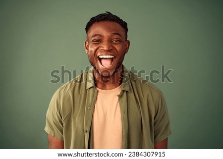 Frank facial expression. Portrait of young african american man smiling cheerfully with open mouth over green background. Handsome guy dressed in casual khaki shirt expressing happiness in studio.
