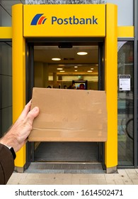 Frankfurt, Germany - Dec 27, 2019: Man Hand Holding Postal Envelope In Front Of Postbank Postal Office In German City POV Personal Perspective