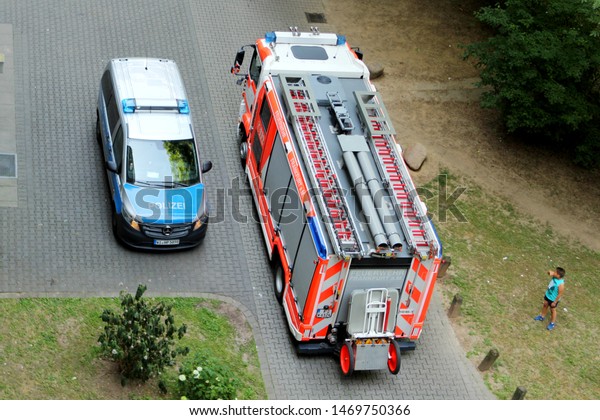 Frankfurt, GERMANY, JUNE 2019: a boy is standing\
and looking at light blue police car stands next to a bright red\
fire truck with an inscription in German language Frankfurt Fire\
Service