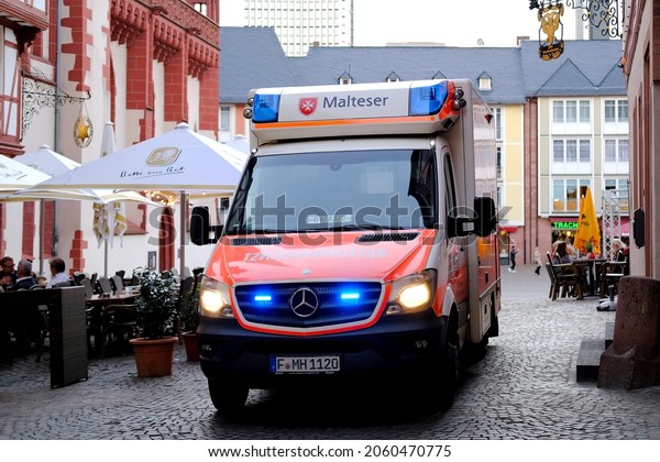 Frankfurt, Germany, October 2021: Red\
Malteser ambulance car with blue lights on in the city center,\
concept of emergency medical care, patient\
transportation