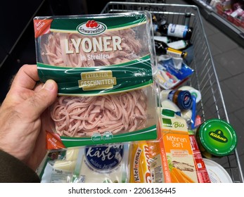 Frankfurt, Germany - Sep 17, 2022: POV Male Hand With Lyoner Meat For Salad Above A Full Shopping Cart Of Groceries At A Convenience Store