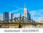 Frankfurt Main Iron footbridge against financial district skyscrapers with blue sky. Skyline cityscape of Frankfurt, Germany during sunny day. Frankfurt is a financial capital of Europe