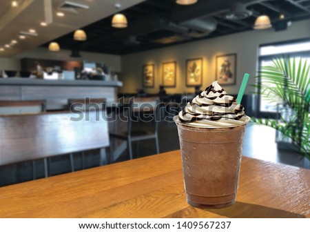 Frappuccino with cream and chocolate sauce in takeaway cup on wooden table