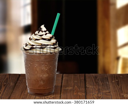 Frappuccino in plastic takeaway or to go cup on wooden table at cafe