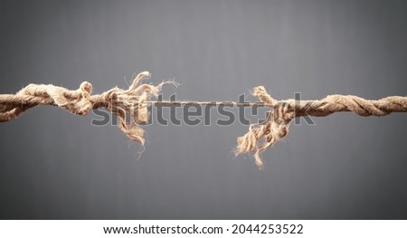 Frayed rope about to break on grey background. Risk