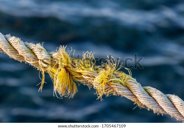 Frayed rope near to break on blue sea water\
background. Selective\
focus.