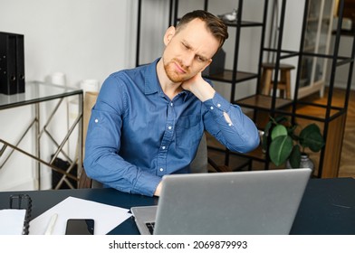 Frazzle guy using laptop for remote working, a guy tired and burnout, holding back of the head and feels ache sitting at the desk in modern office with eyes closed. Overwork concept